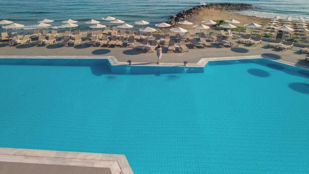 Un espace piscine avec des chaises longues et des parasols, une vue dégagée sur la mer et une côte rocheuse.