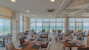 Une salle à manger spacieuse, dotée de grandes fenêtres donnant sur la mer, et aménagée avec des tables et des chaises au design moderne.