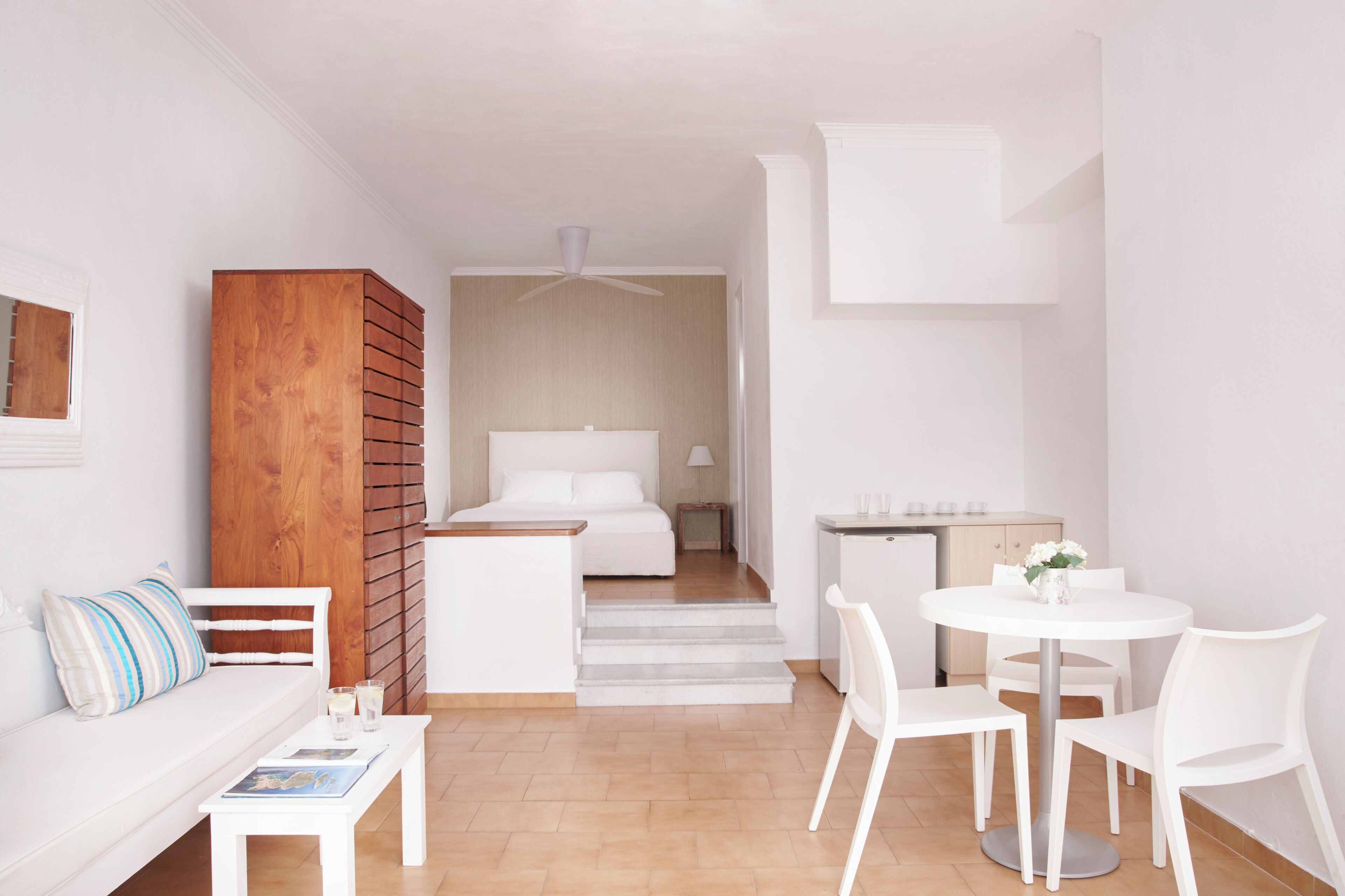 A compact hotel room with a bed, a small kitchenette, a dining area with a table and chairs, and a sofa.