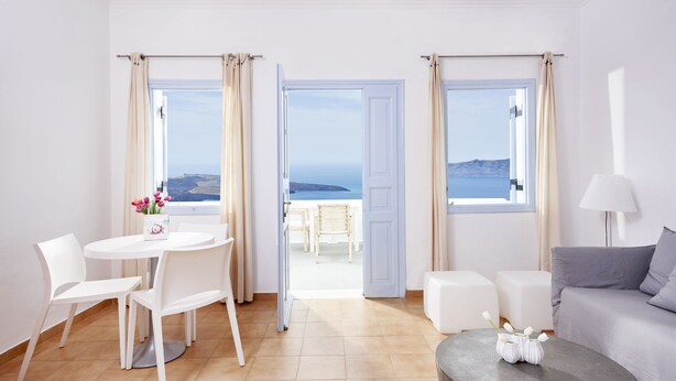 A modern room with a dining area, a sofa, and a view of the sea. - Manos Small World (Santorini)