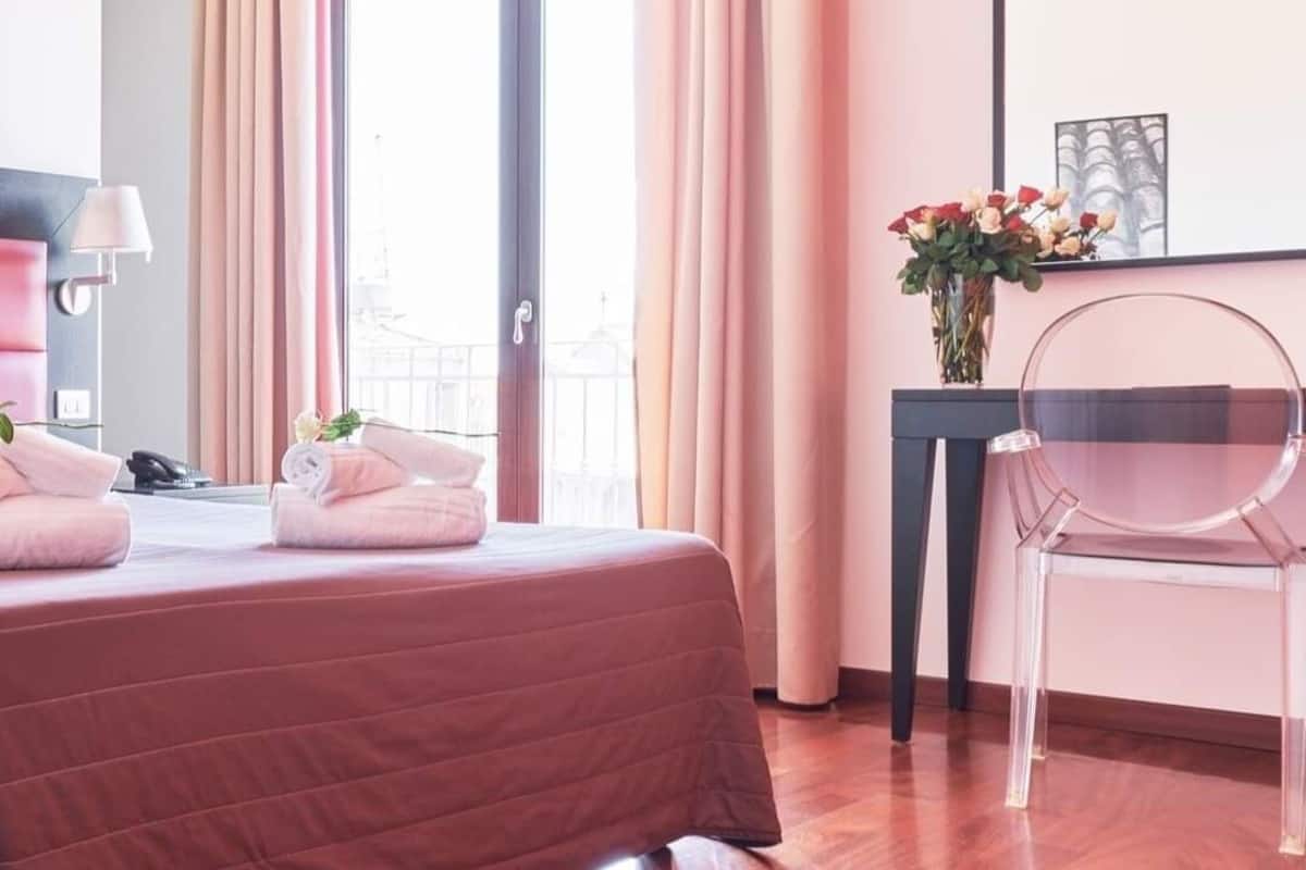 A hotel room with a bed, a desk, a chair, and a window with curtains.