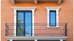 Fachada de edificio con dos ventanas, cada una con marco blanco y barandilla de balcón negra.