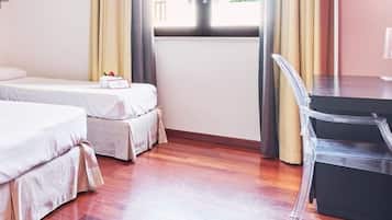 Habitación de hotel con dos camas, un escritorio, una silla y una ventana con cortinas.