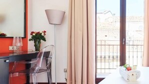 Una habitación de hotel con cama, escritorio, silla, lámpara y ventana con cortinas.