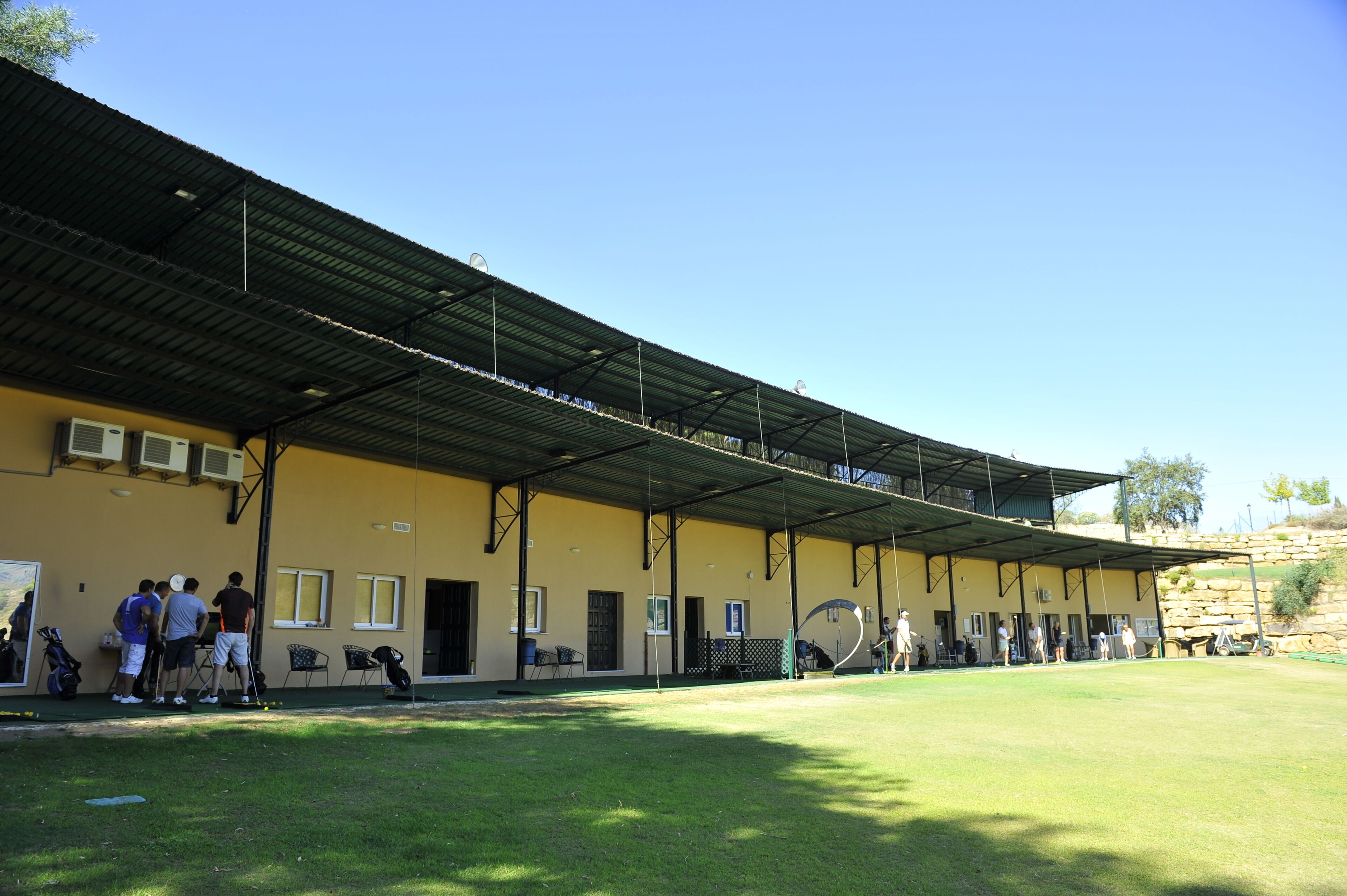 A building with a flat roof, multiple windows, and a covered area with chairs and tables.