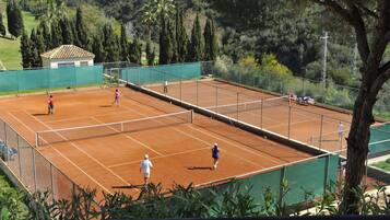Una cancha de tenis con una red, rodeada por una valla y árboles al fondo.