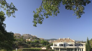 Ein großes, modernes Gebäude mit Pool und Springbrunnen, umgeben von üppiger Vegetation und blauem Himmel.