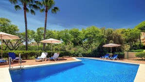 Ein Swimmingpool mit Liegestühlen und Sonnenschirmen, umgeben von Palmen und Grünpflanzen.