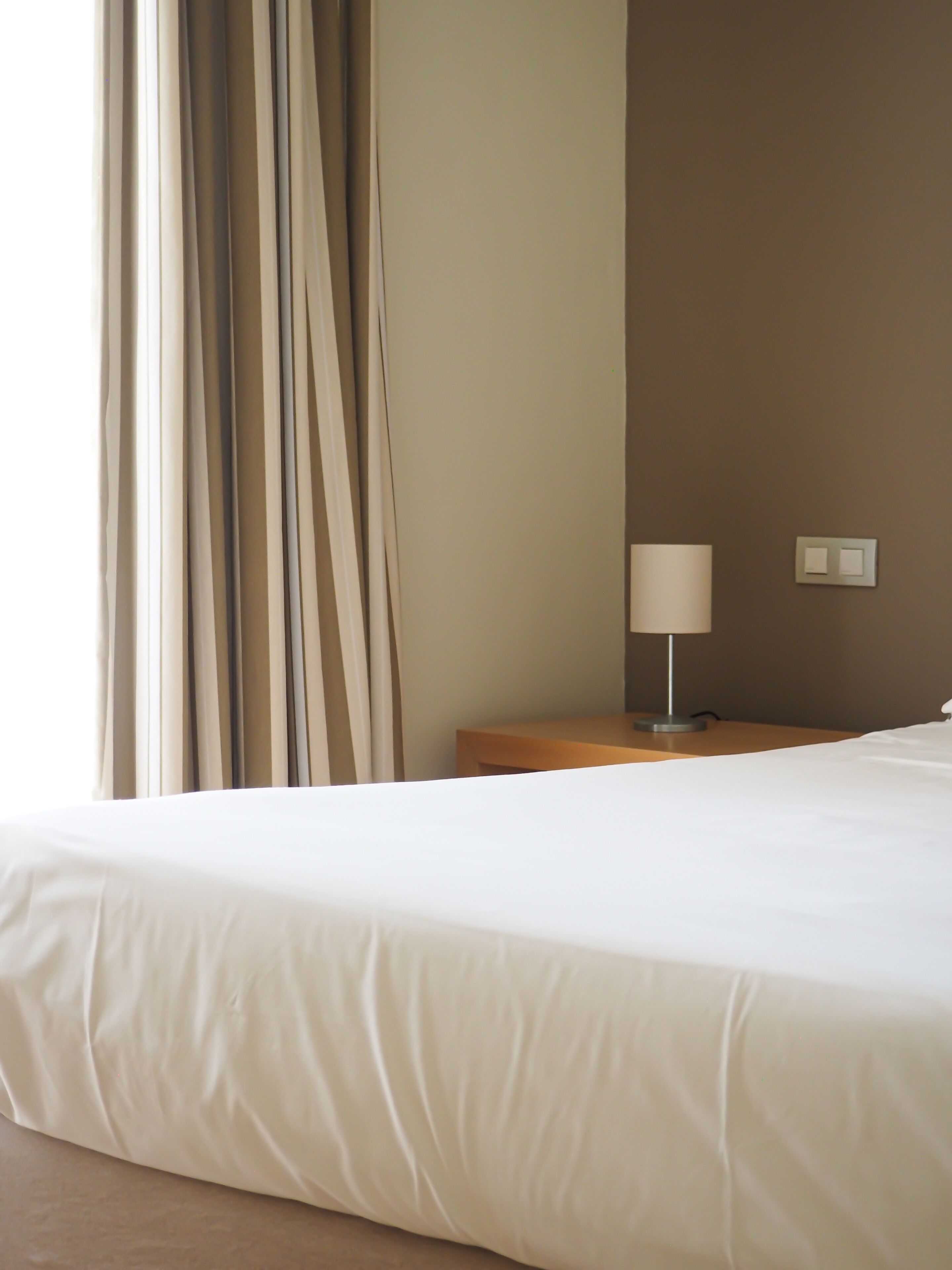 Et hotelværelse med en seng, et natbord, en lampe og en vægkontakt.