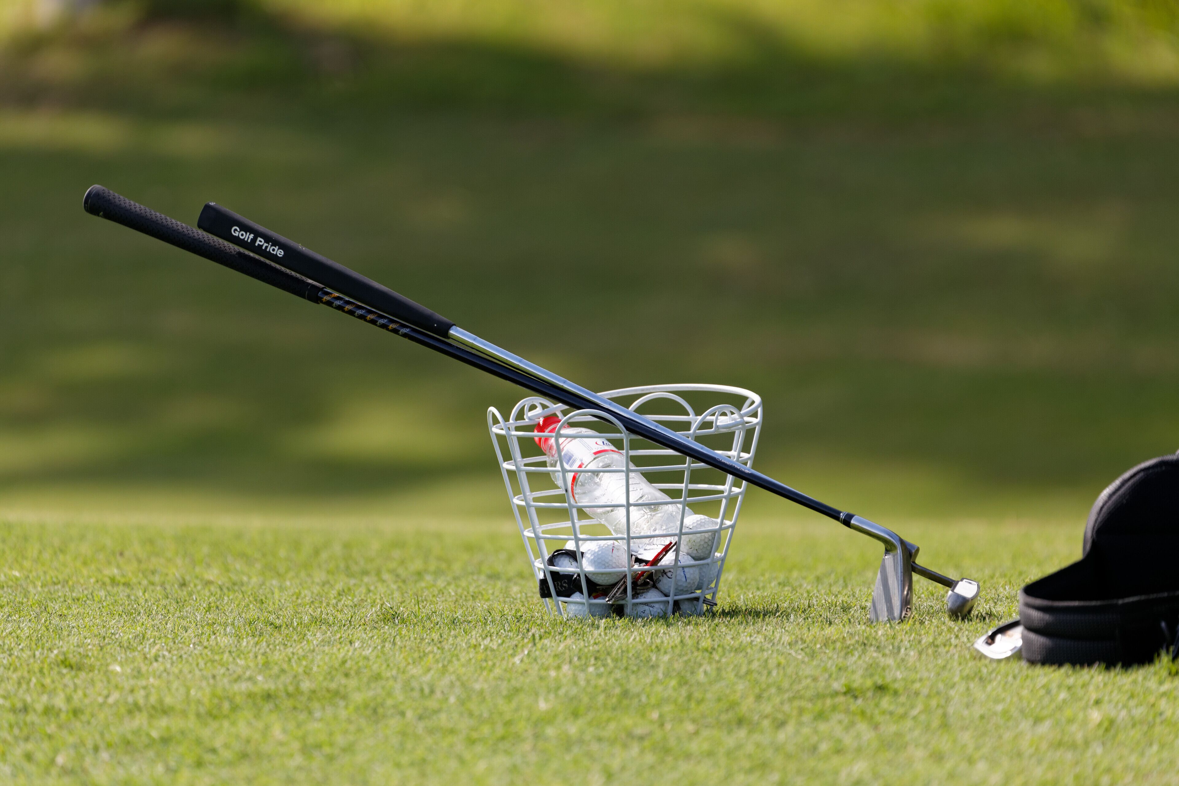 A golf club and balls in a basket on a grassy field.
