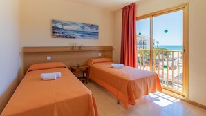 A hotel room with two beds, a painting, a nightstand, and a balcony with a view of the beach and buildings. - Apartamentos Pins Marina Cambrils (Cambrils)