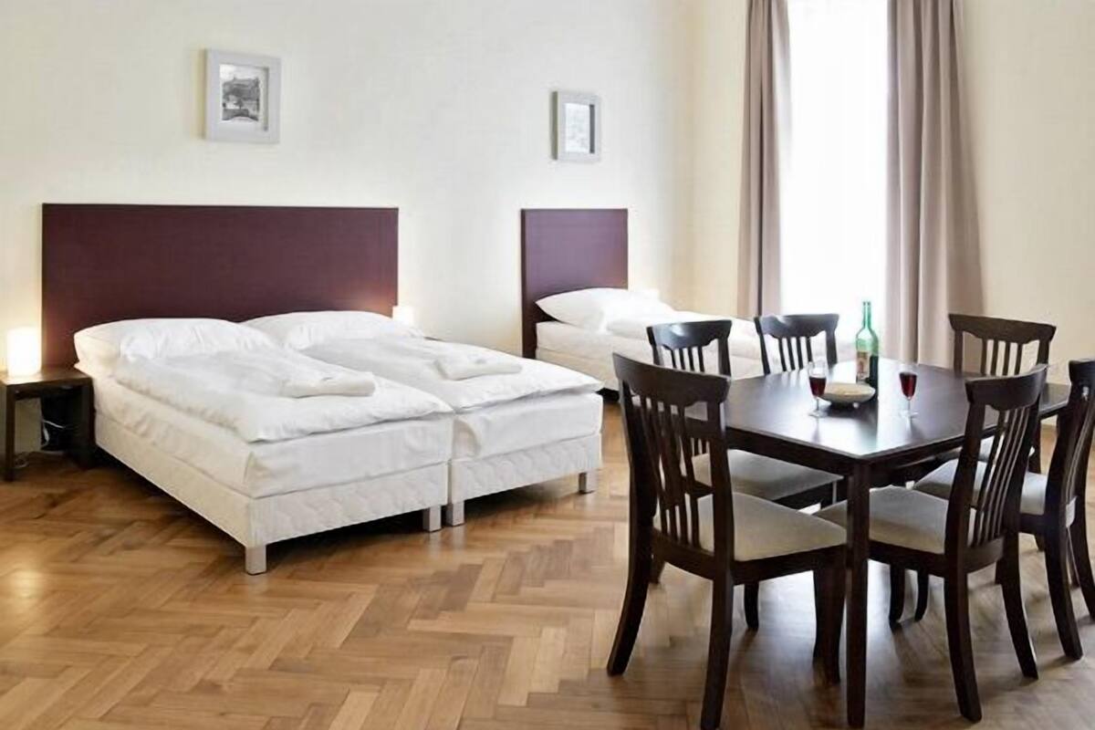 A hotel room with a double bed, a small table with chairs, and a wooden herringbone floor.