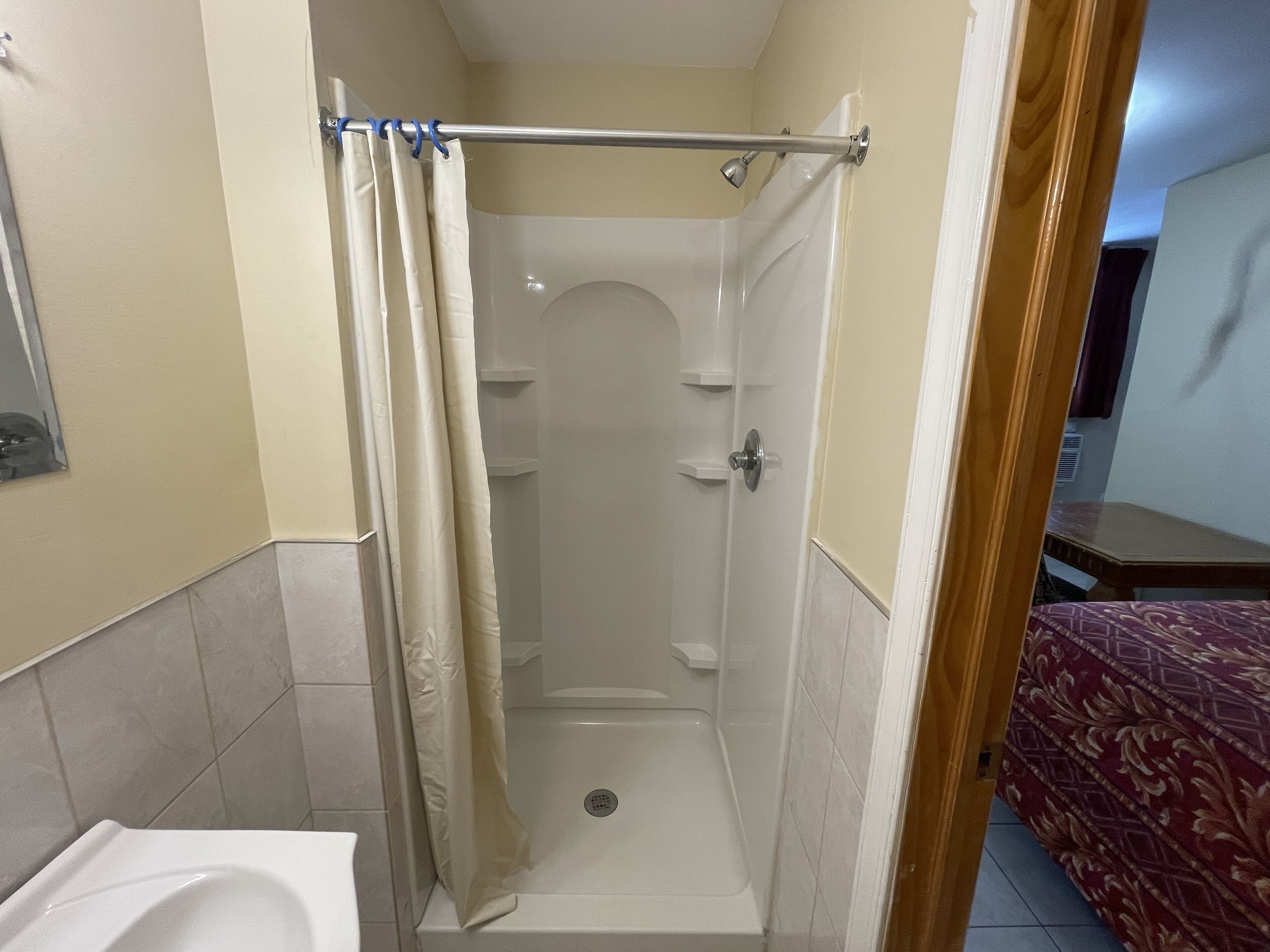Ein kleiner, abgeschlossener Duschbereich mit Duschvorhang, einer weißen Badewanne und einer Tür zu einem anderen Raum.