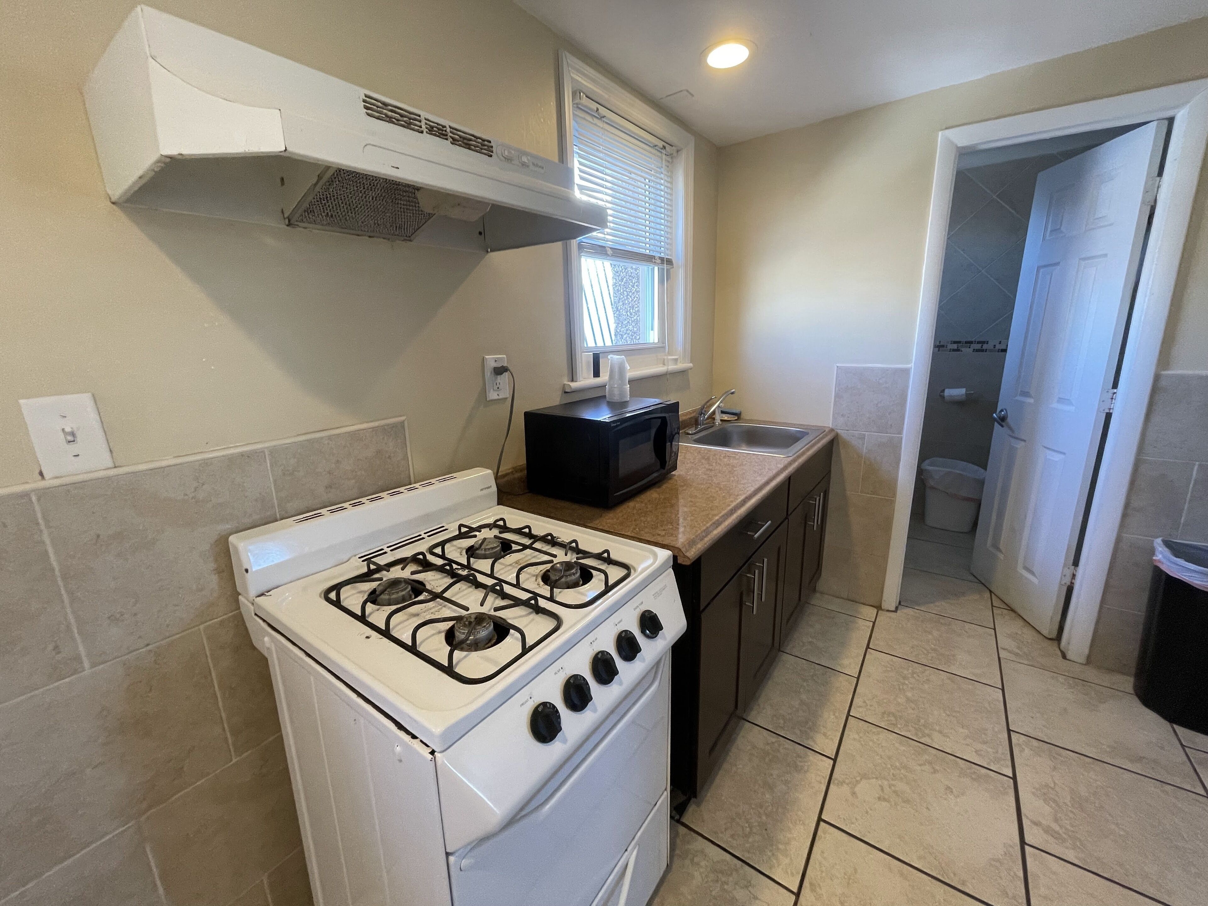 A kitchen with a gas stove, a microwave, a sink, and a window with blinds.