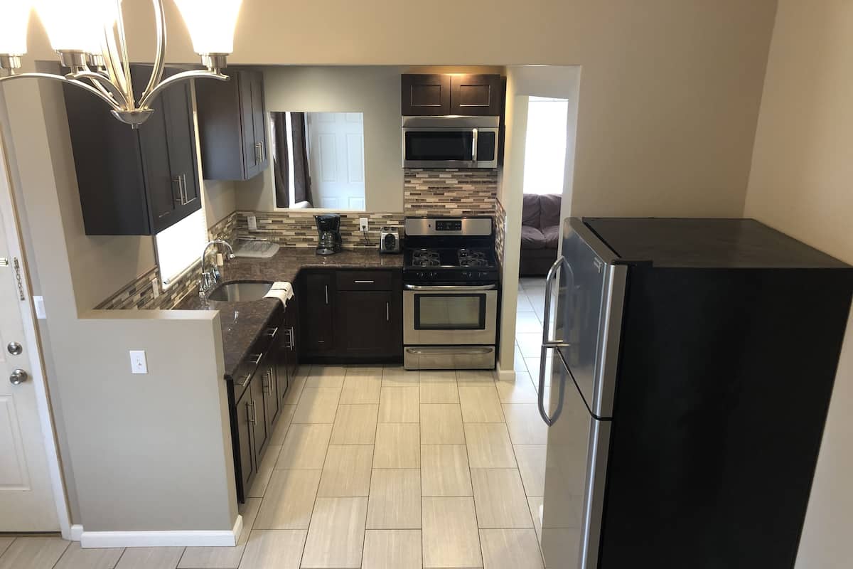 A modern kitchen with dark cabinets, a stainless steel refrigerator, a built-in oven, and a microwave.
