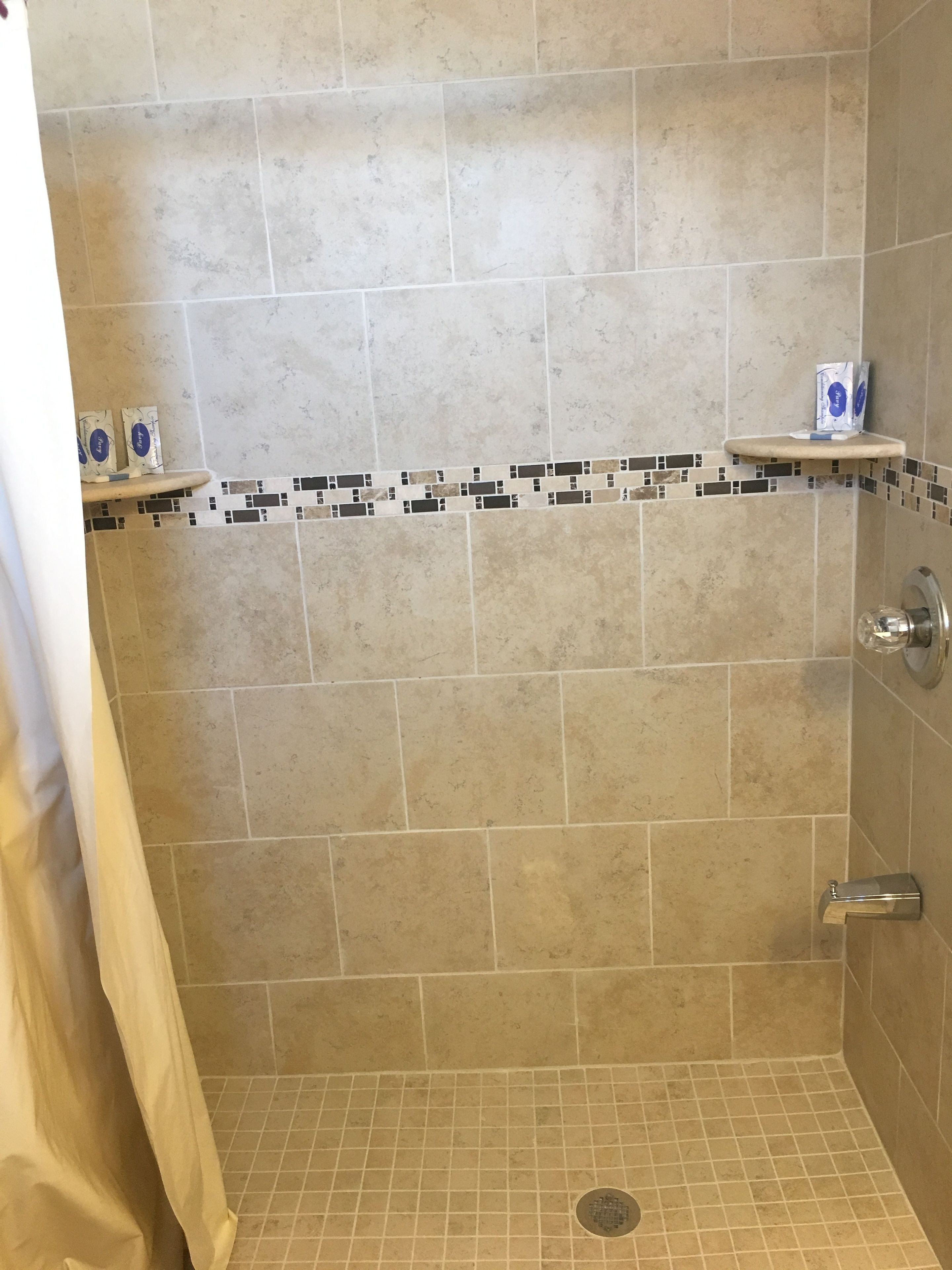 Zona de ducha con azulejos color beige, un estante pequeño con artículos de aseo y mando de ducha.