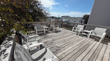 A wooden deck with white chairs and a table, overlooking a residential area.