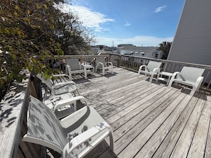 A wooden deck with white chairs and a table, overlooking a residential area.