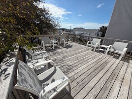 Una terraza de madera con sillas y una mesa blancos, con vistas a una zona residencial.