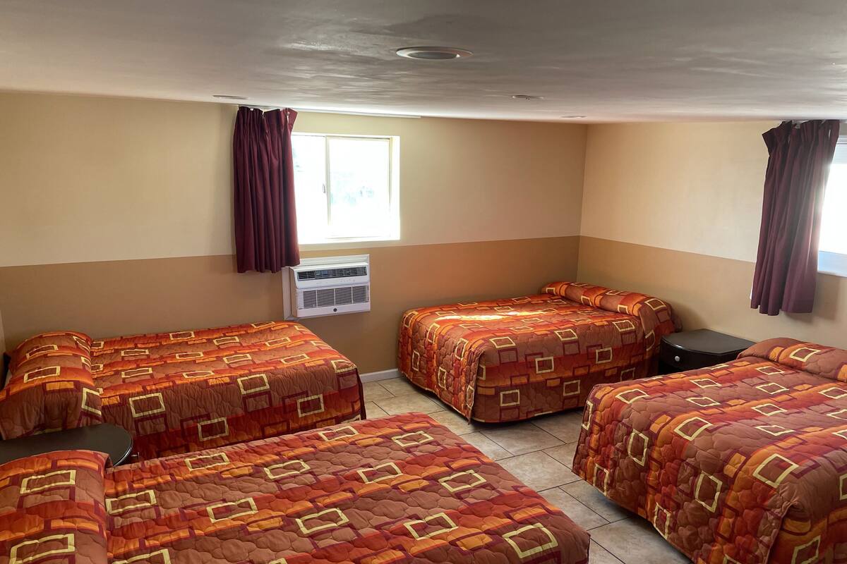 A hotel room with four beds, a window with curtains, an air conditioning unit, and a tiled floor.
