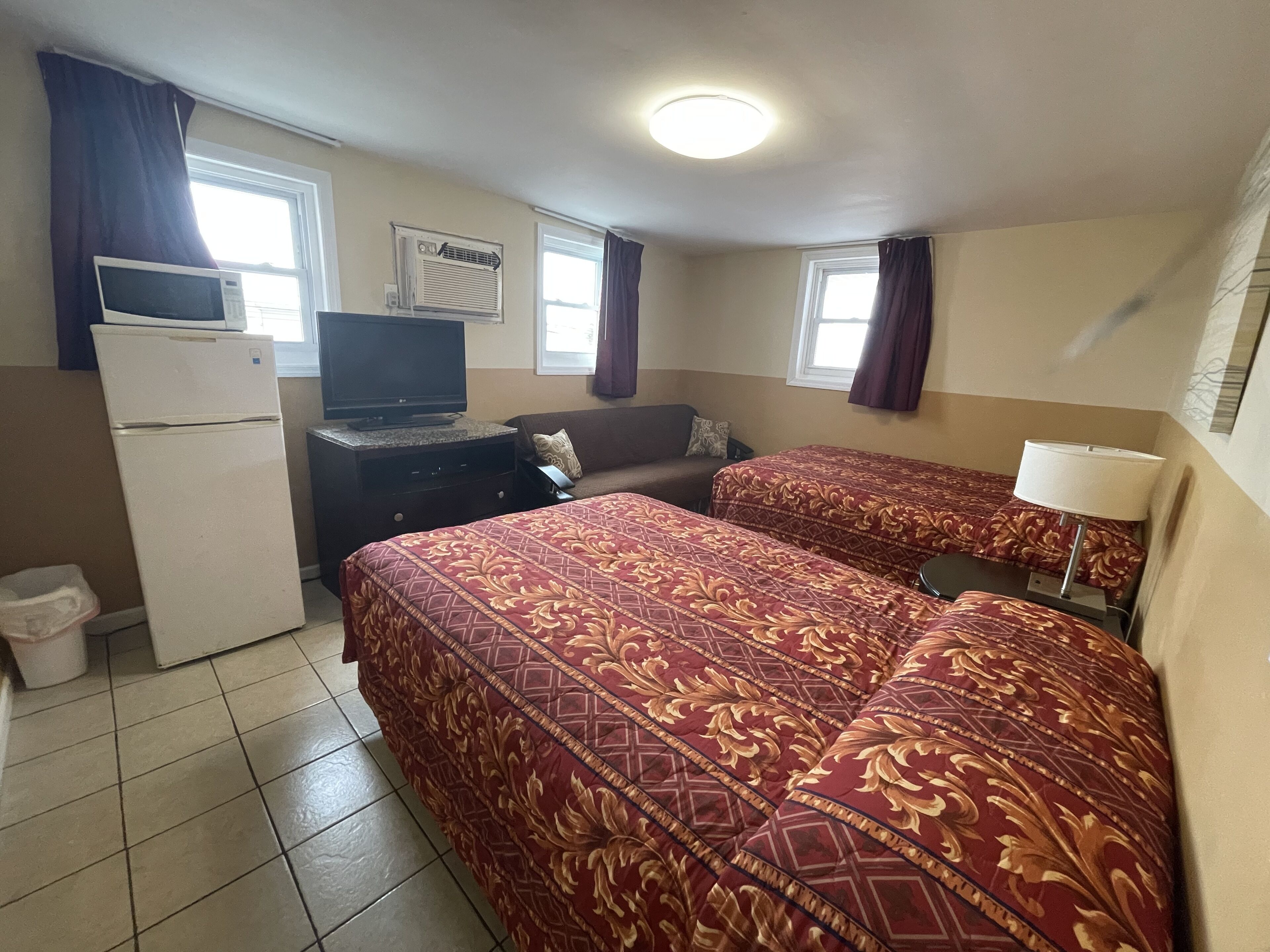 Une chambre d’hôtel avec deux lits, un réfrigérateur, une télévision, un bureau et une fenêtre avec des rideaux.