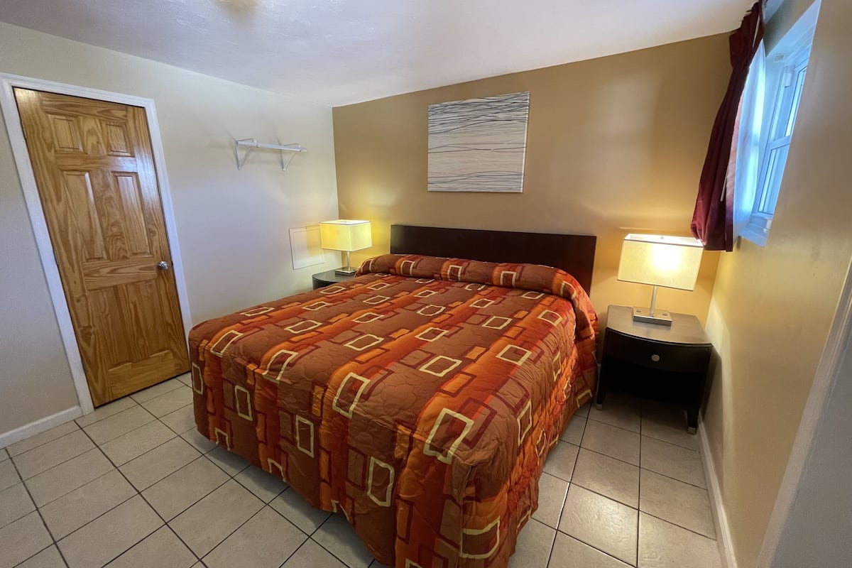 A hotel room with a large bed, two bedside tables with lamps, a wooden door, and a window with curtains.