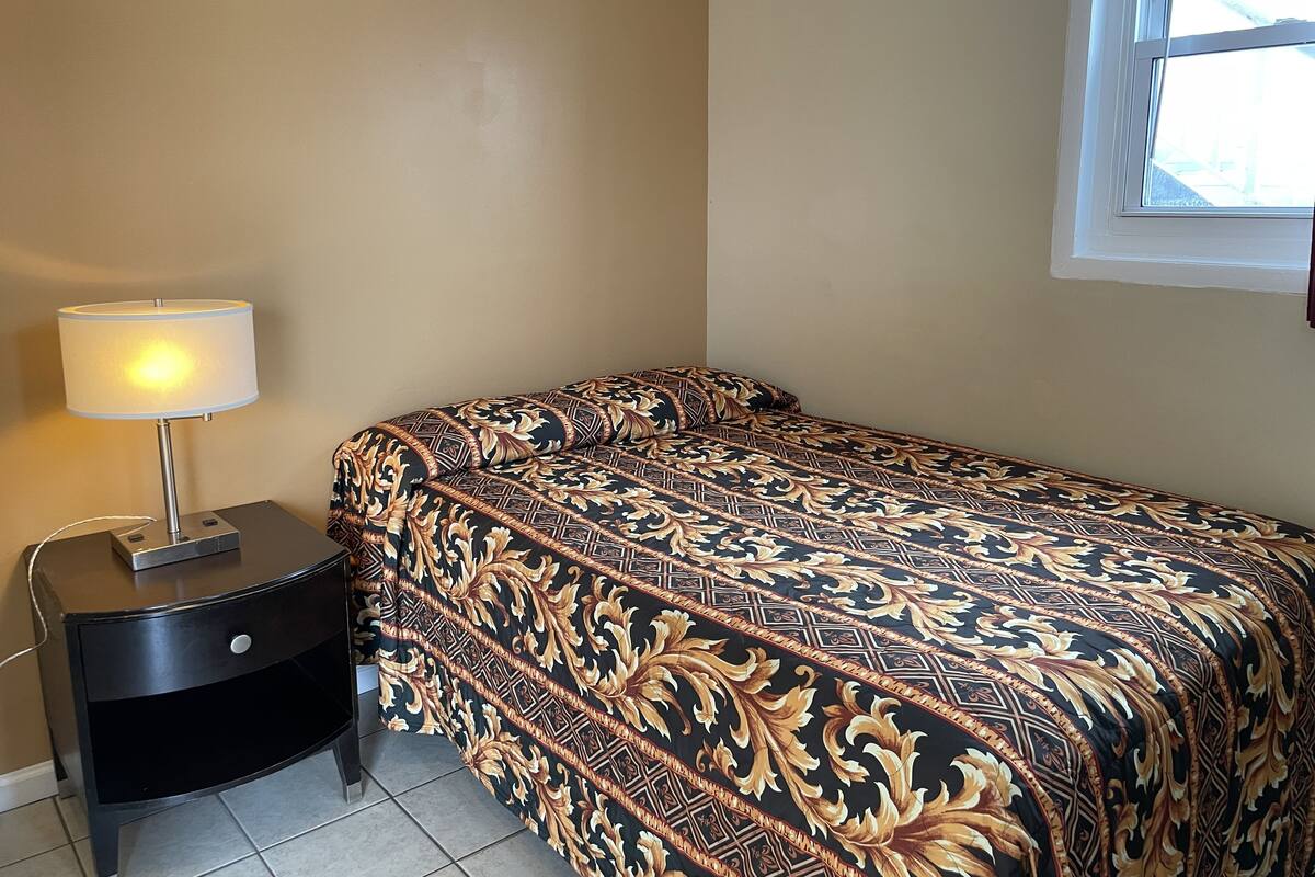A bedroom with a bed, a nightstand, a lamp, and a window.