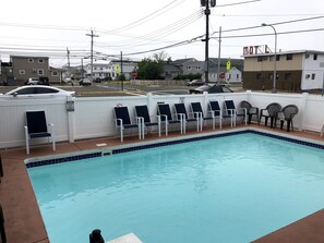 A swimming pool with lounge chairs and a white fence. - Anchor Motel (Seaside Heights)