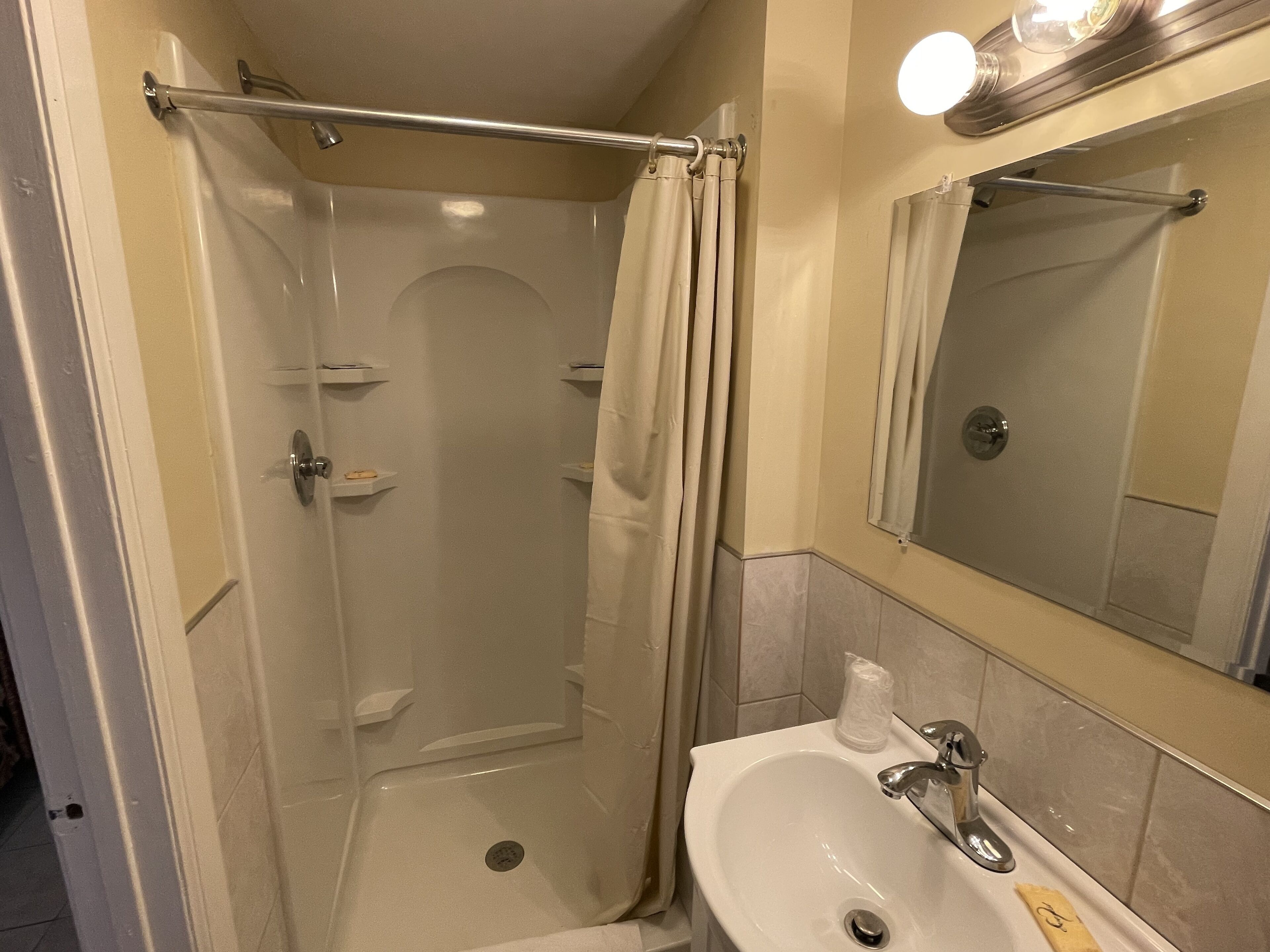 Un baño pequeño con ducha, lavamanos y espejo.