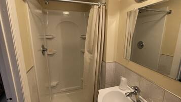 Un baño pequeño con ducha, lavamanos y espejo.