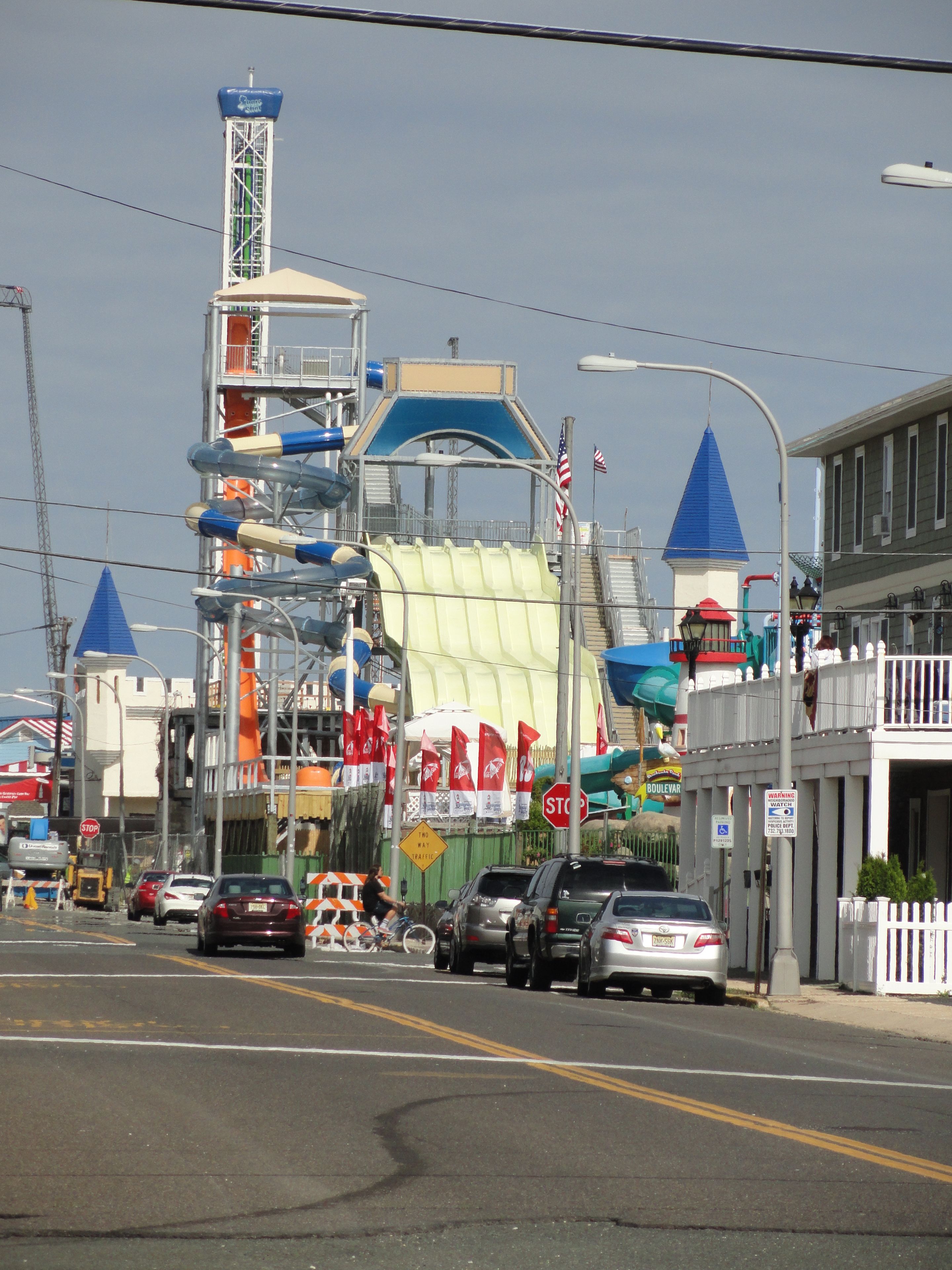 A street with cars parked on the side, a water tower, and a building with a blue roof.
