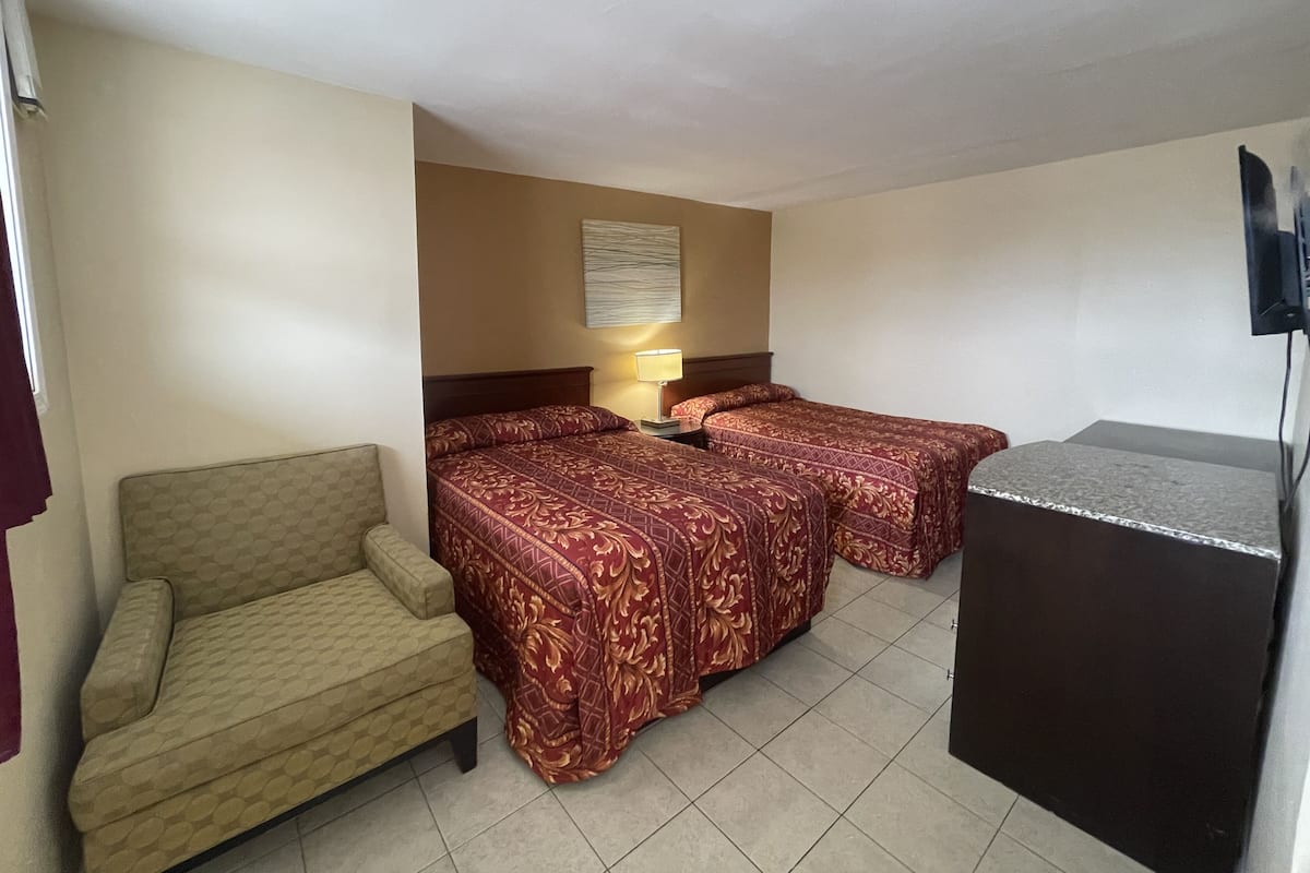A hotel room with two beds, a sofa, a TV, and a lamp.