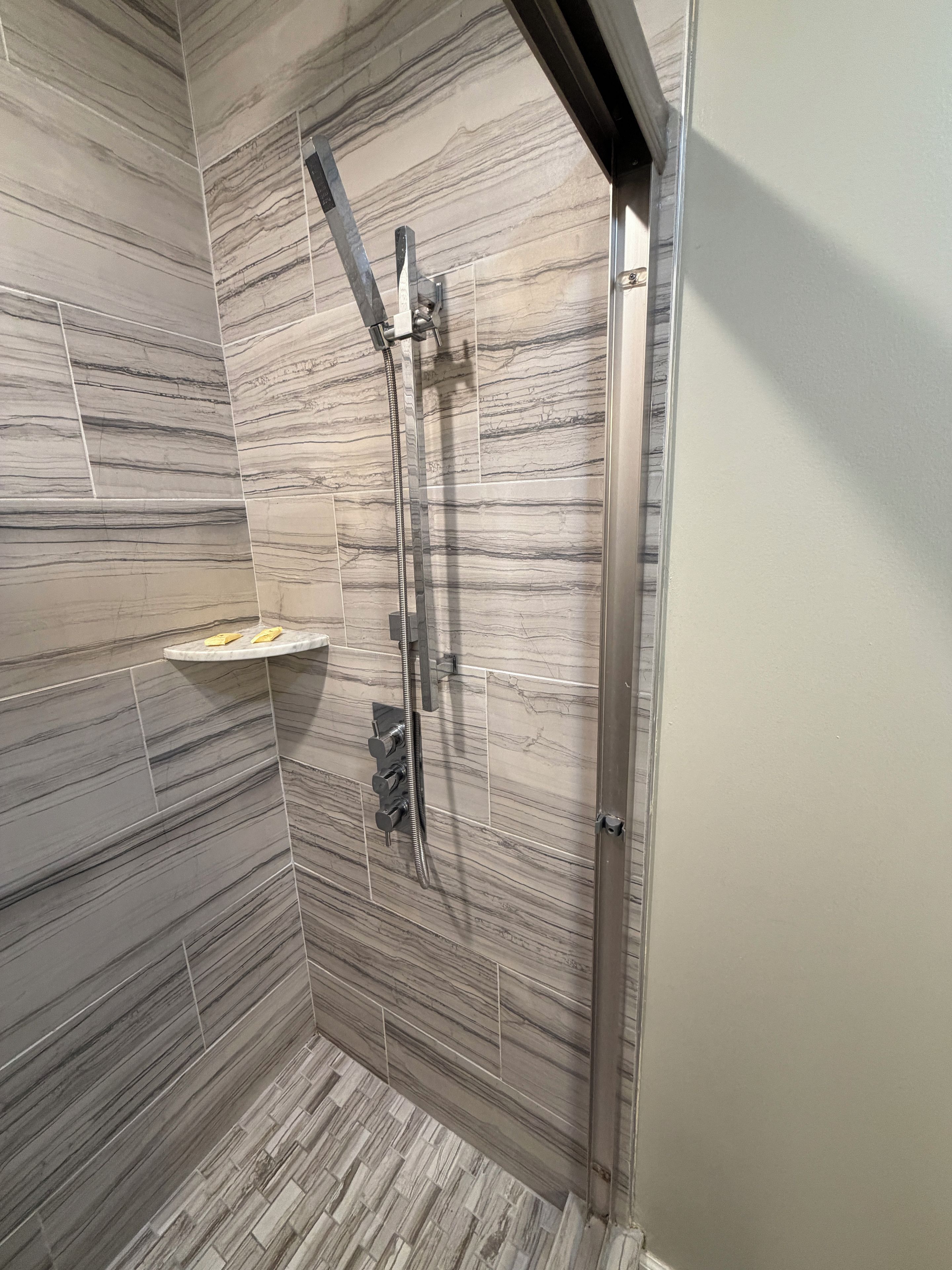 A shower with a handheld showerhead and a wall-mounted control panel.