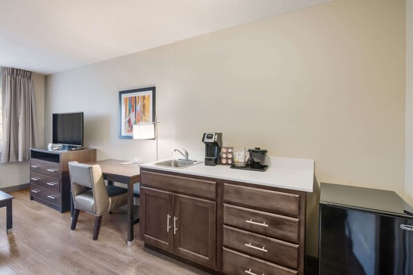 A compact hotel room with a kitchenette, a dining area, and a television.