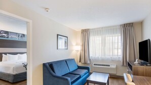 A hotel room with a bed, a blue sofa, a small table, a TV, and a window with curtains. - Sleep Inn & Suites Columbus near Fort Benning (Columbus)