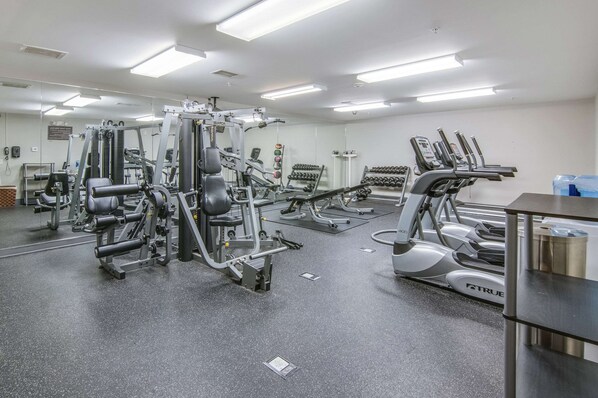Un gimnasio con diferentes máquinas de ejercicio, un espejo grande y un ambiente limpio y bien iluminado.
