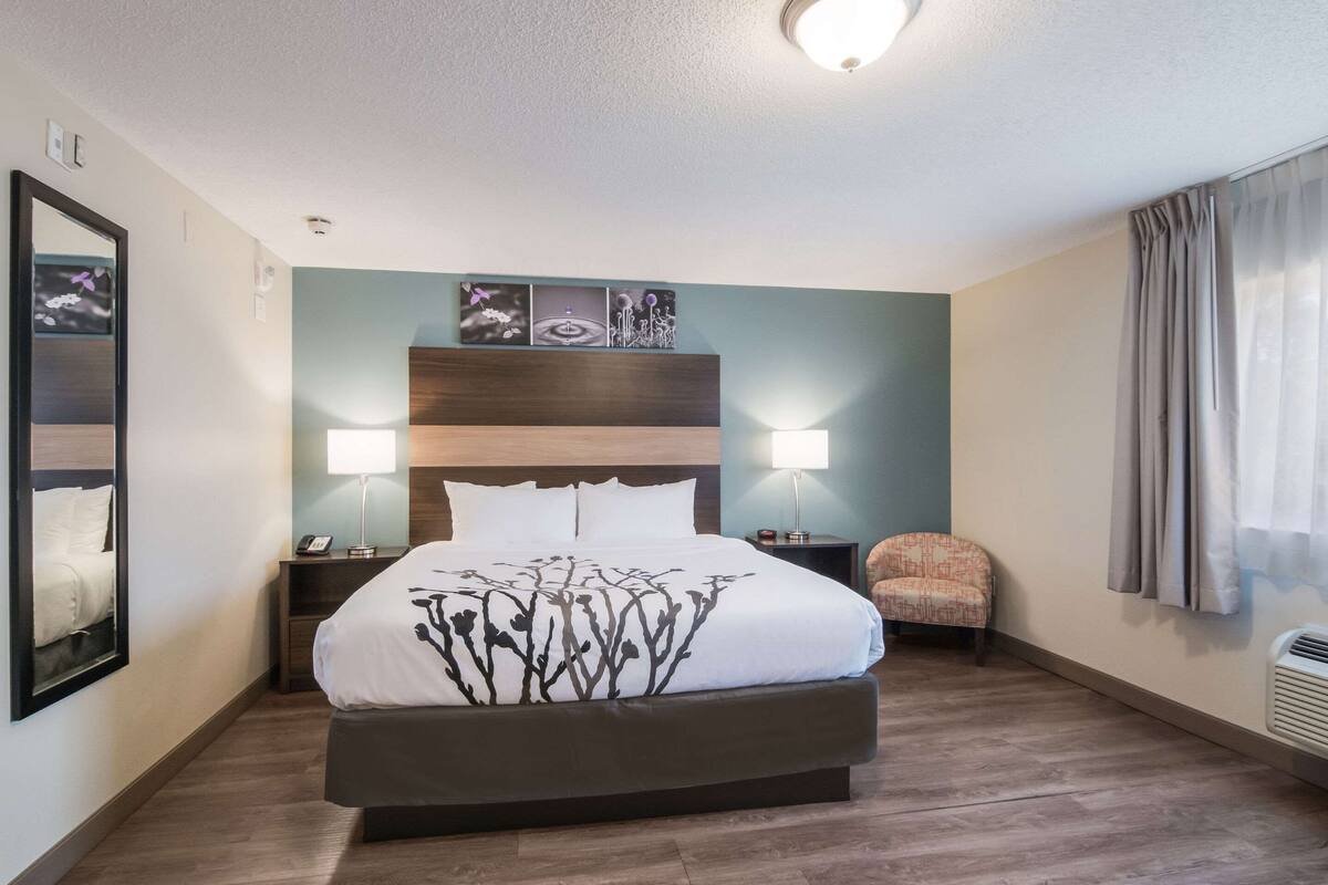 A hotel room with a large bed, two bedside tables, a chair, and artwork on the wall.