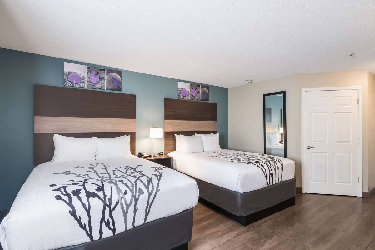 A hotel room with two beds, a nightstand with a lamp, and a door.