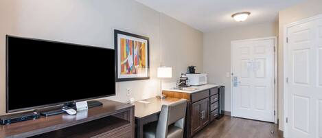 A hotel room with a flat-screen TV, a desk with a lamp, a microwave, and a dining area.
