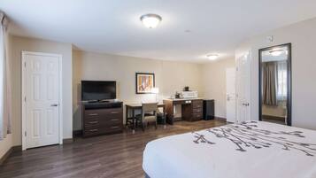 A hotel room with a bed, a desk with a chair, a television, a microwave, and a door.