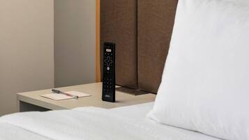A hotel room with a bed, a nightstand, a remote control, a wall-mounted lamp, and a pillow.