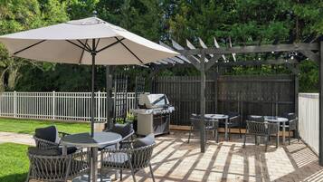 An outdoor patio area with a pergola, a grill, and seating arrangements.