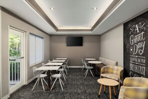 Un salón de conferencias con televisor de pantalla plana, varias mesas, sillas y un amplio ventanal con persianas.