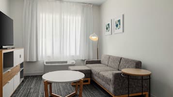 Moderni hotellihuone, jossa on sohva, pyöreä pöytä, televisio, lamppu ja patteri.