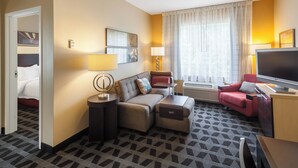 Hotellihuone, jossa on sohva, televisio, työpöytä ja ikkuna, jossa on verhot.