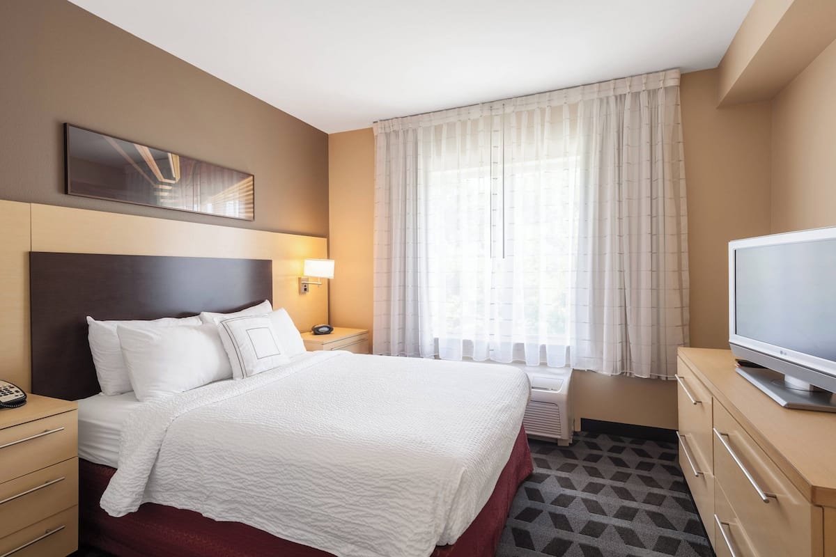 Une chambre d’hôtel avec un grand lit, une télévision, une table de chevet, une lampe et une fenêtre avec des rideaux.
