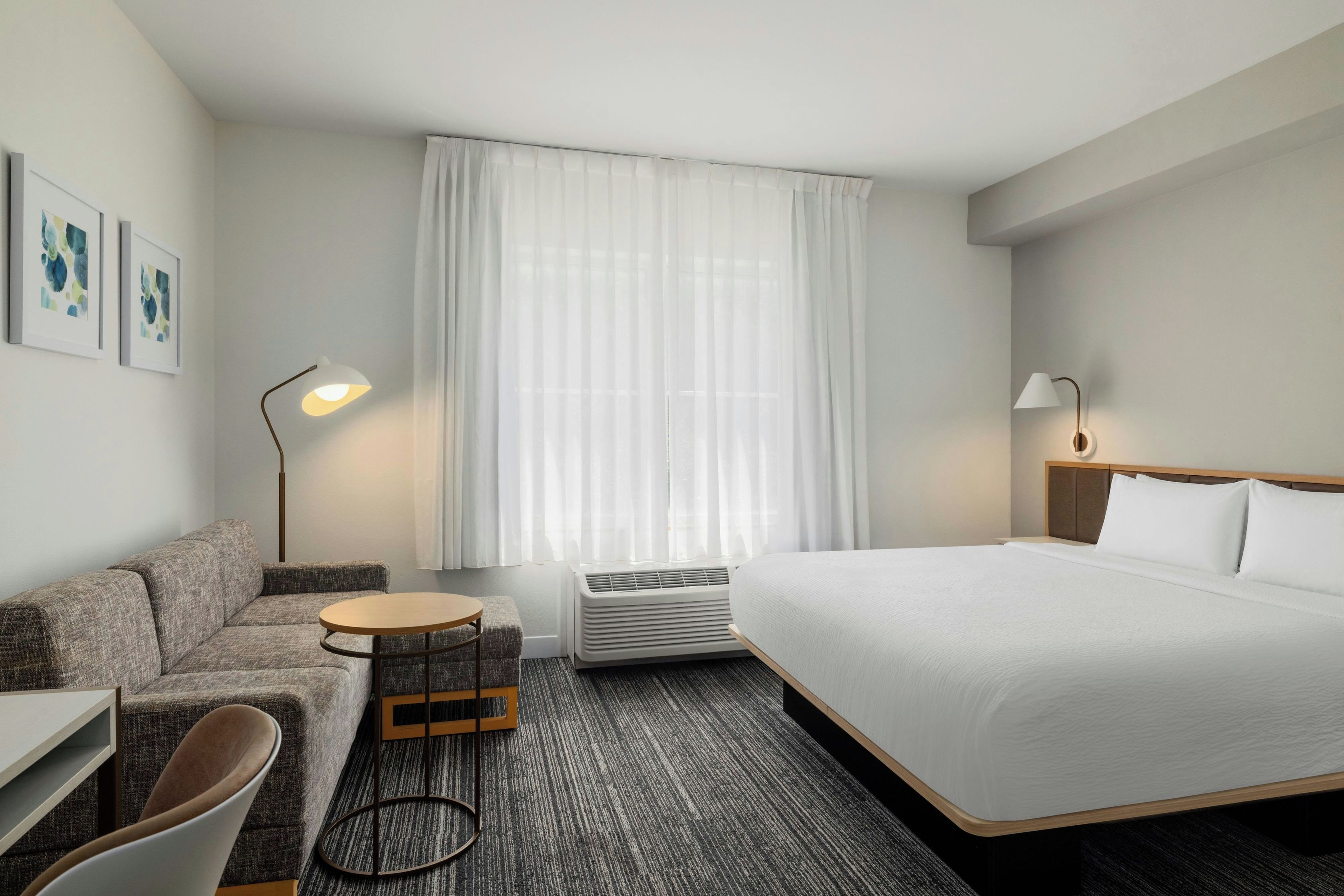 Una camera d'albergo con un letto, un divano, un tavolino, una sedia, una scrivania, una lampada e una finestra con tende.