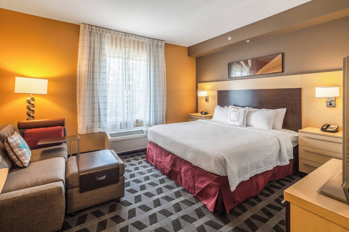 Une chambre d’hôtel avec un grand lit, un canapé, un bureau et une fenêtre avec des rideaux.