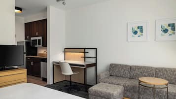 A modern hotel room with a bed, a desk with a chair, a sofa, a small round table, and artwork on the wall.
