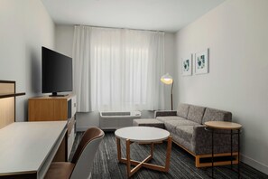 Habitación de hotel con televisión de pantalla plana, sofá, mesa redonda y lámpara.